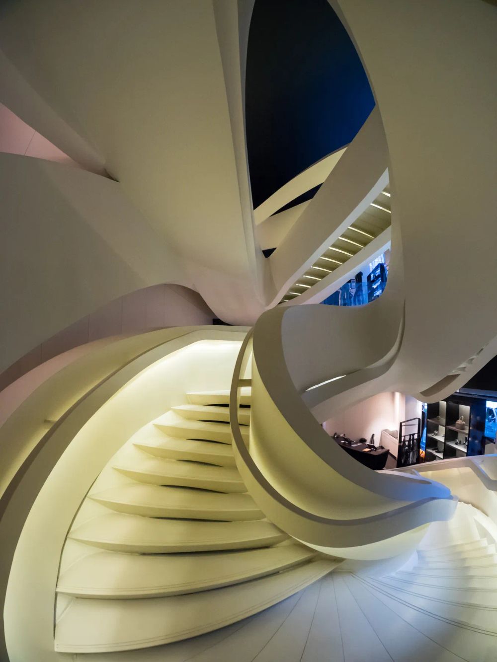 An illuminated sculptural stair curling through a softly colored interior