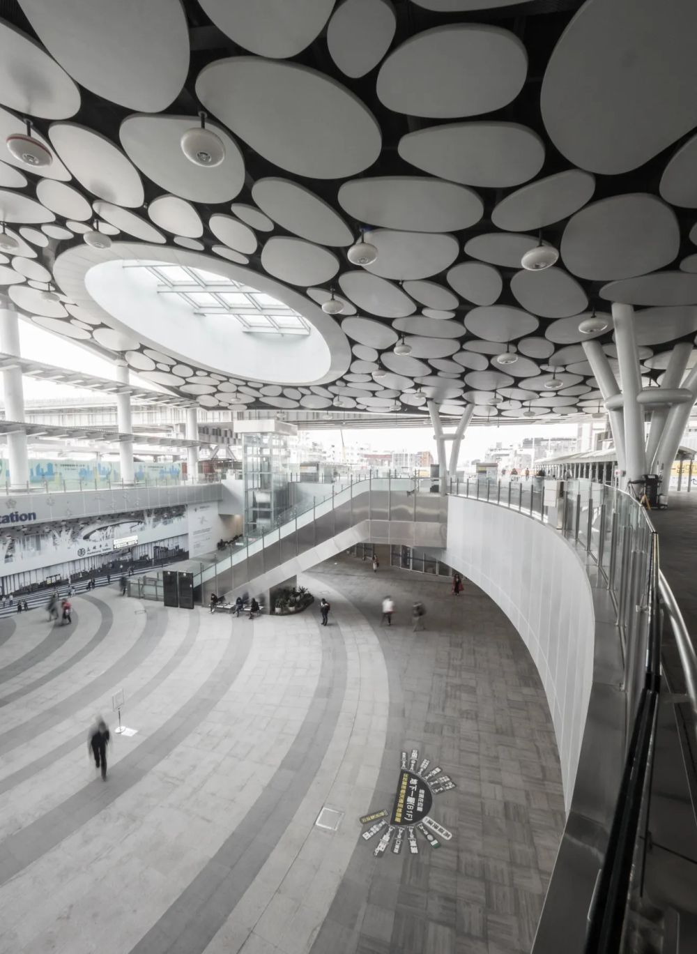 Circular ceiling panels above a curving concourse and a blurred pedestrian