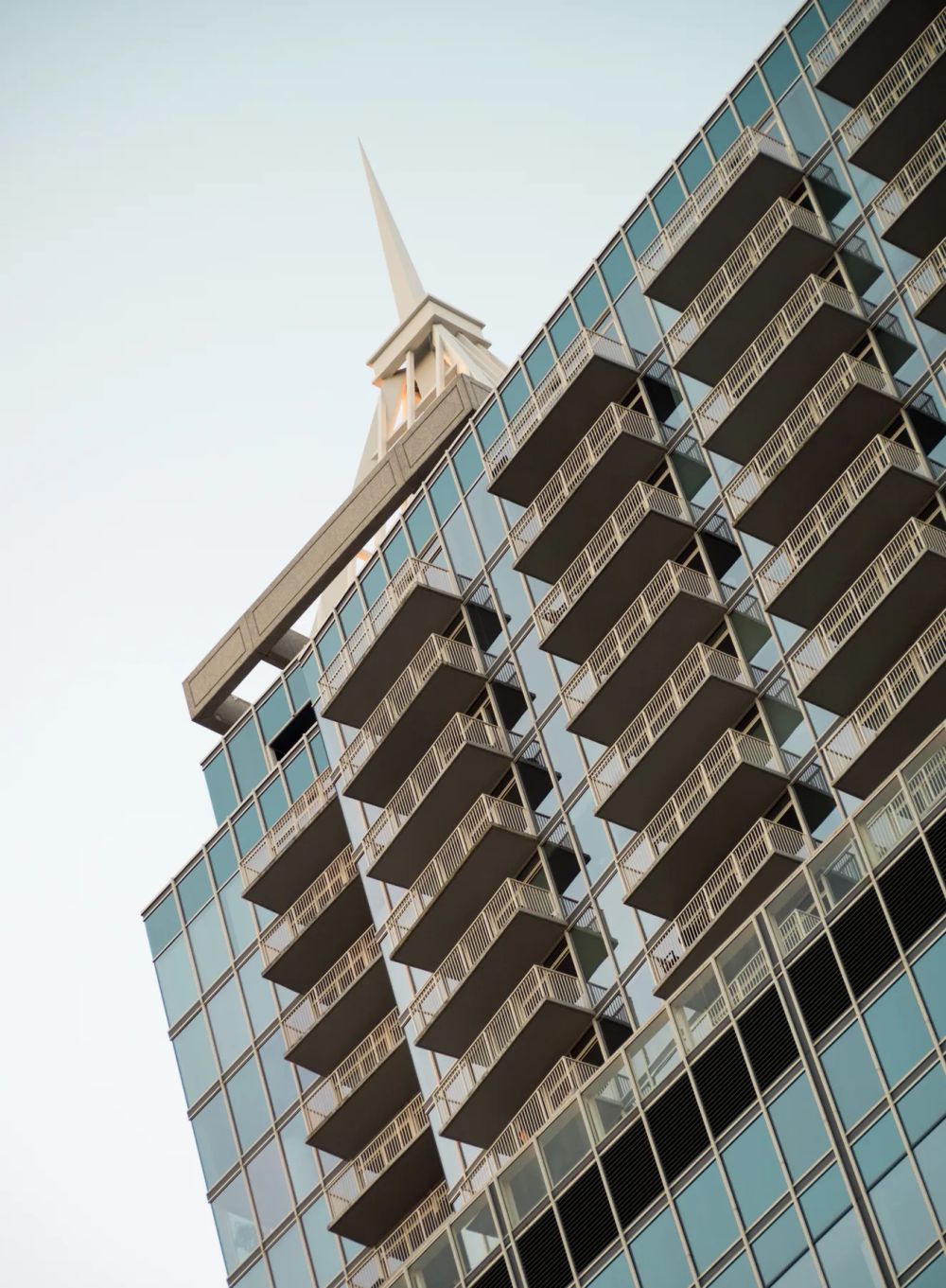 Stacked balconies projecting from a glass building viewed from below