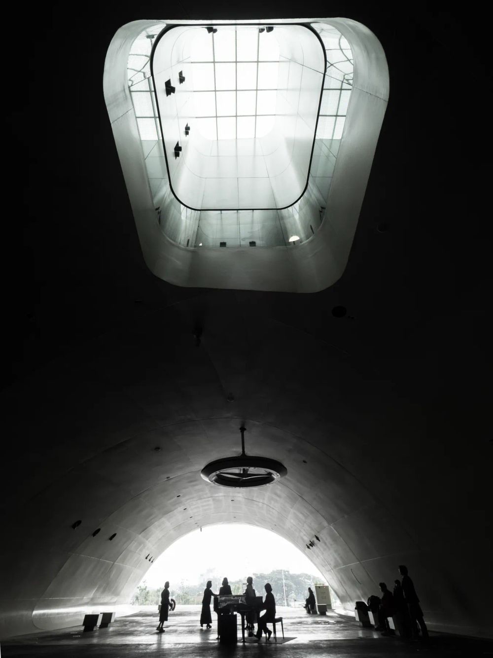 People silhouetted beneath a bright opening in a dark sculptural interior