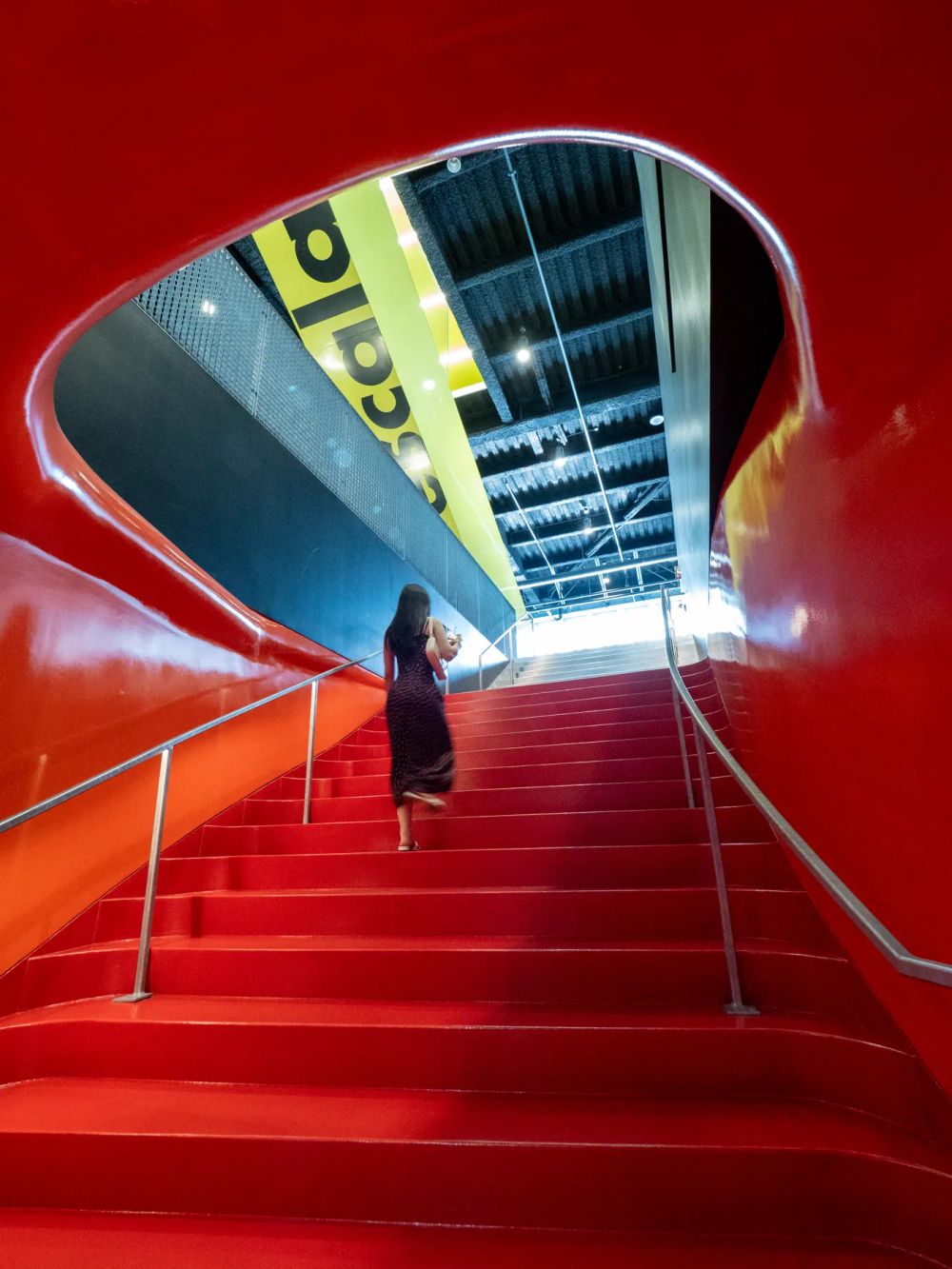 A red stair rising toward a blue opening with a small figure on the steps