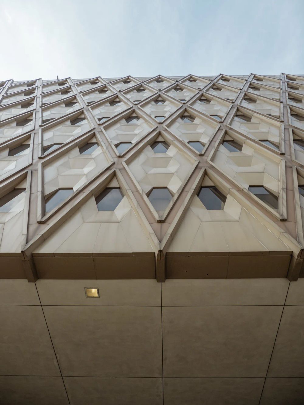 A sculpted concrete screen with repeated diagonal openings viewed from below