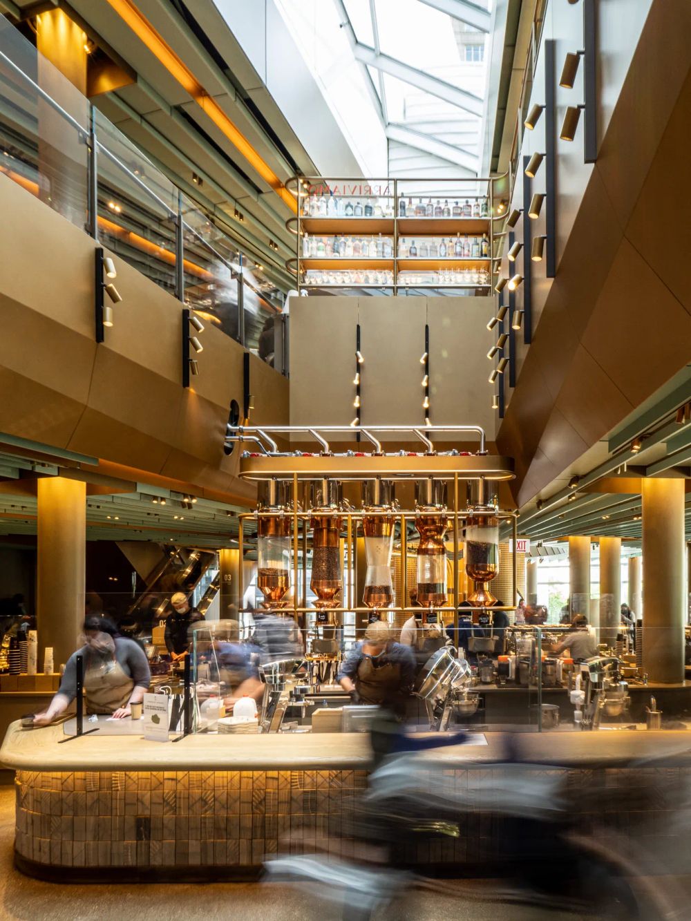 Blurred customers at a counter beneath a tall skylit commercial atrium
