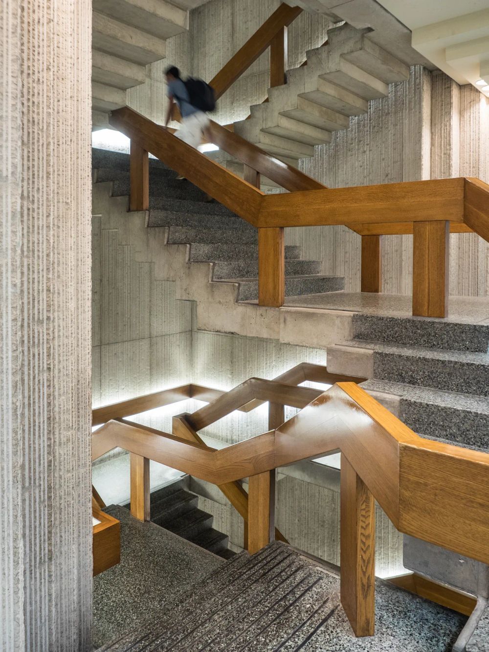 A person moving along concrete stairs with timber handrails