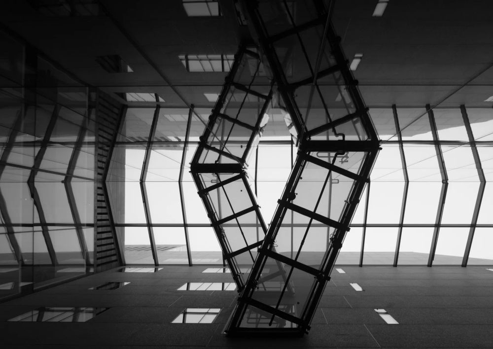 A dark angular structure reflected in the glass wall of a gallery