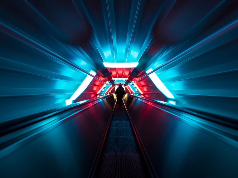 Blue and red light streaks converging along an escalator