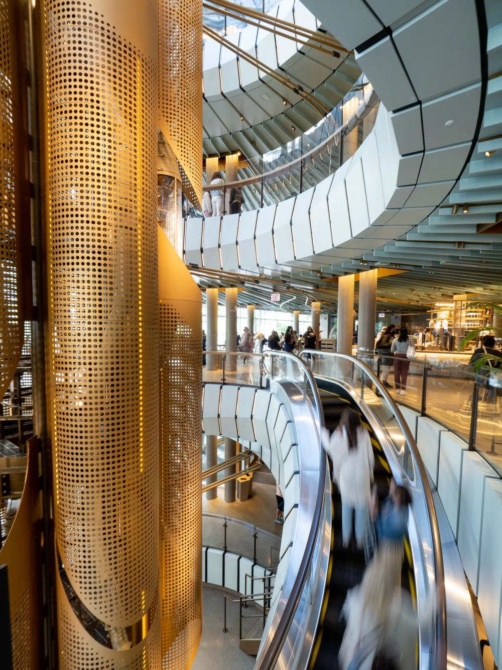 Blurred passengers on a curved escalator beside a tall golden metal core