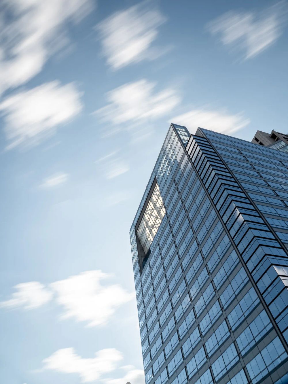 Streaked white clouds above the sharp corner of a glass tower