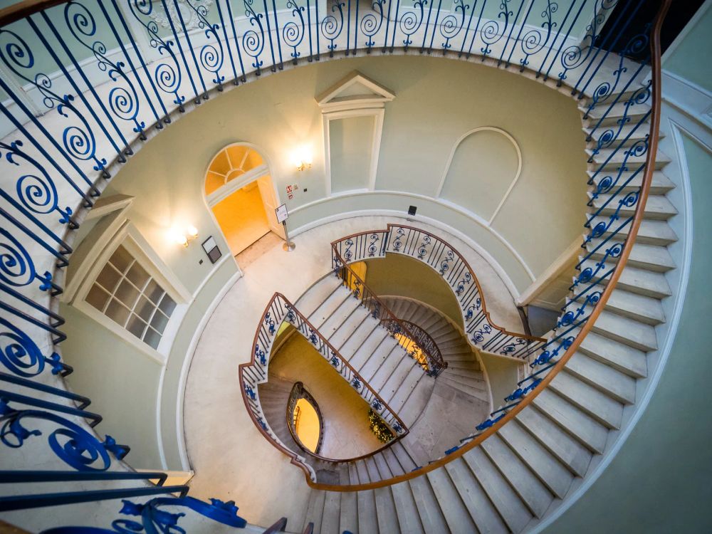 An ornate spiral stair with blue iron railings viewed from above