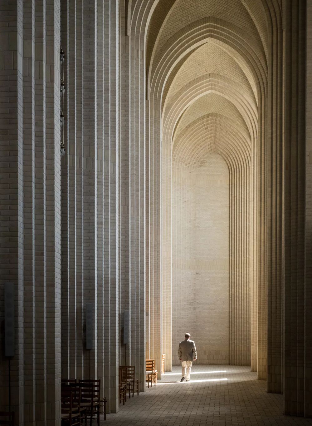 A lone figure beneath tall repeated brick arches in warm light
