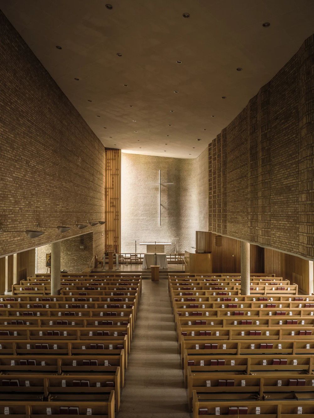Rows of wooden pews facing a softly lit altar between tall brick walls