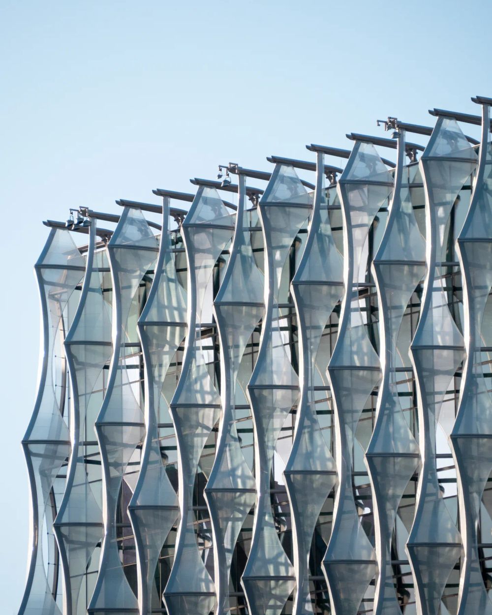 Repeating bowed glass bays and steel supports against a pale blue sky