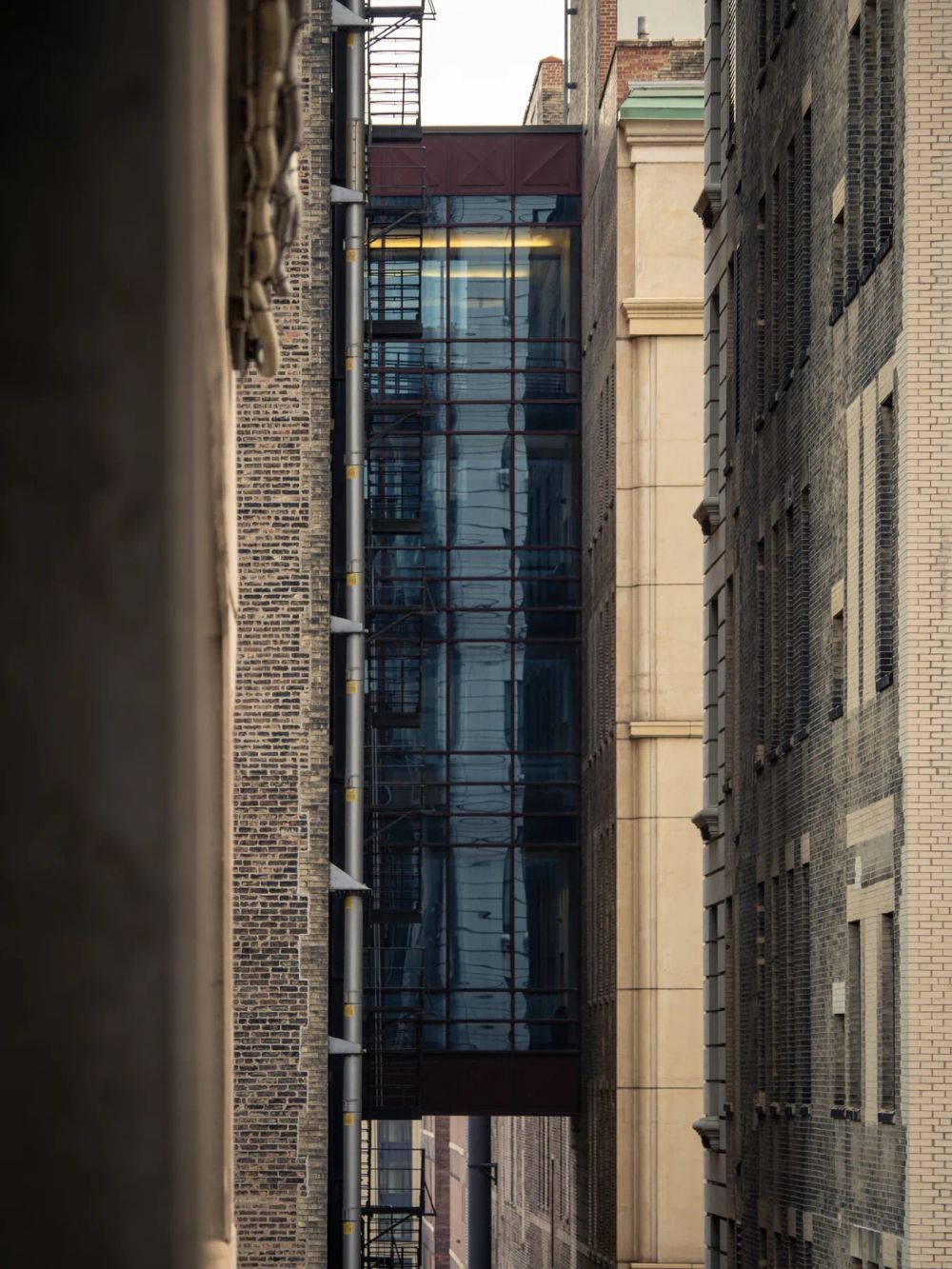 A narrow glass skybridge suspended between two older masonry buildings