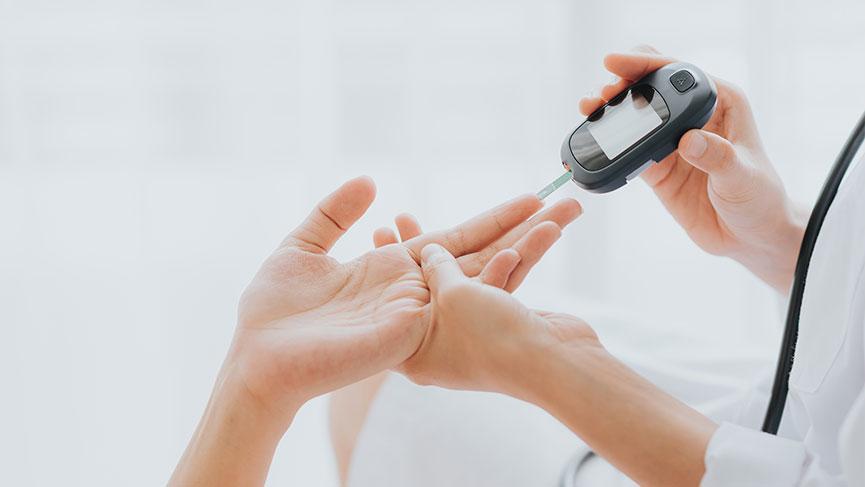 Gloved hand holding a blood glucose meter to a fingertip
