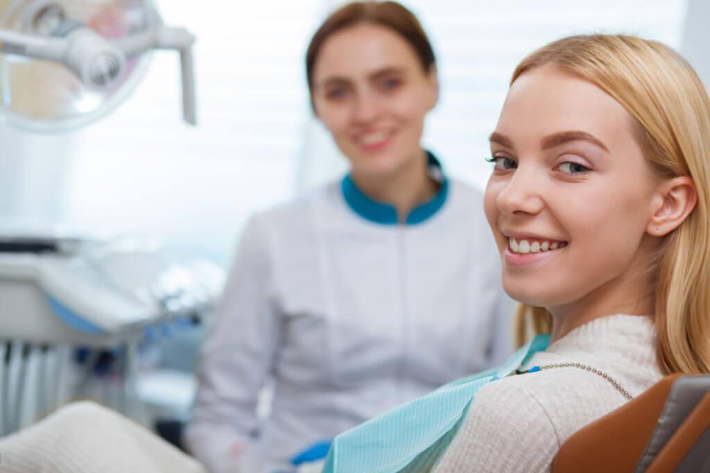 Smiling young woman in a dental chair with a dentist behind her