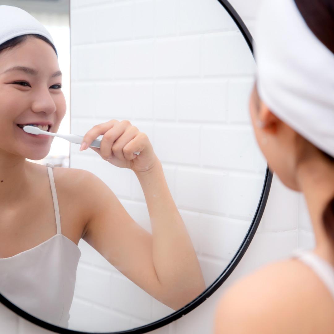 Smiling woman brushing her teeth at a mirror