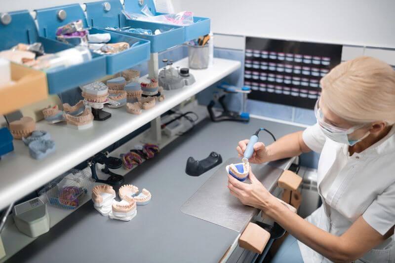 Dental technician working on a tooth model in a laboratory with plaster models on shelves