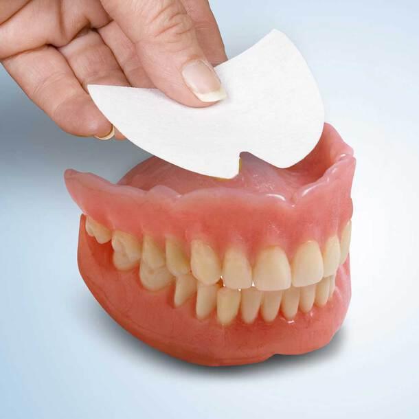 Hand placing an adhesive pad onto a denture