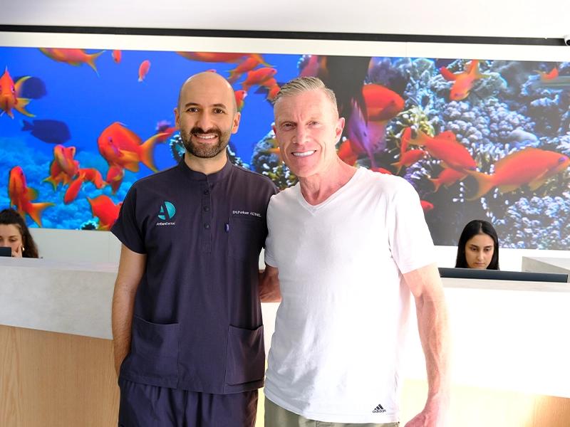 Dentist and a smiling man standing in front of a fish wall display