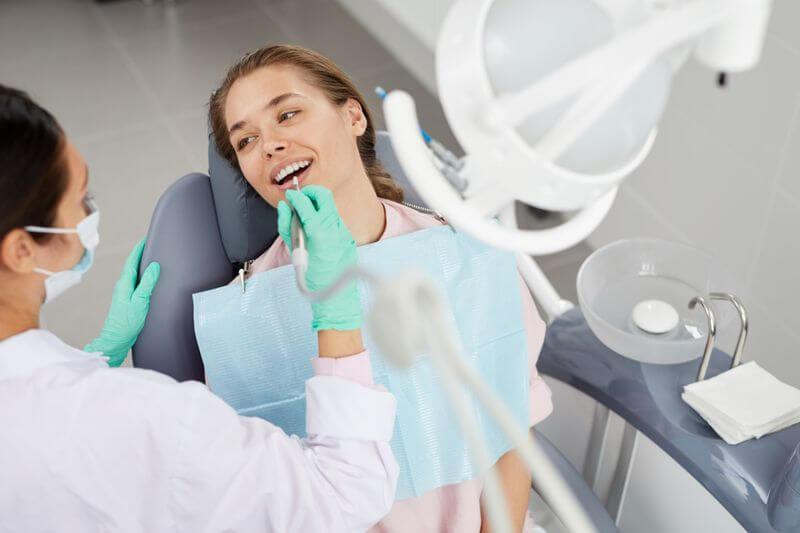 Dentist in mask and green gloves examining a smiling patient in the chair