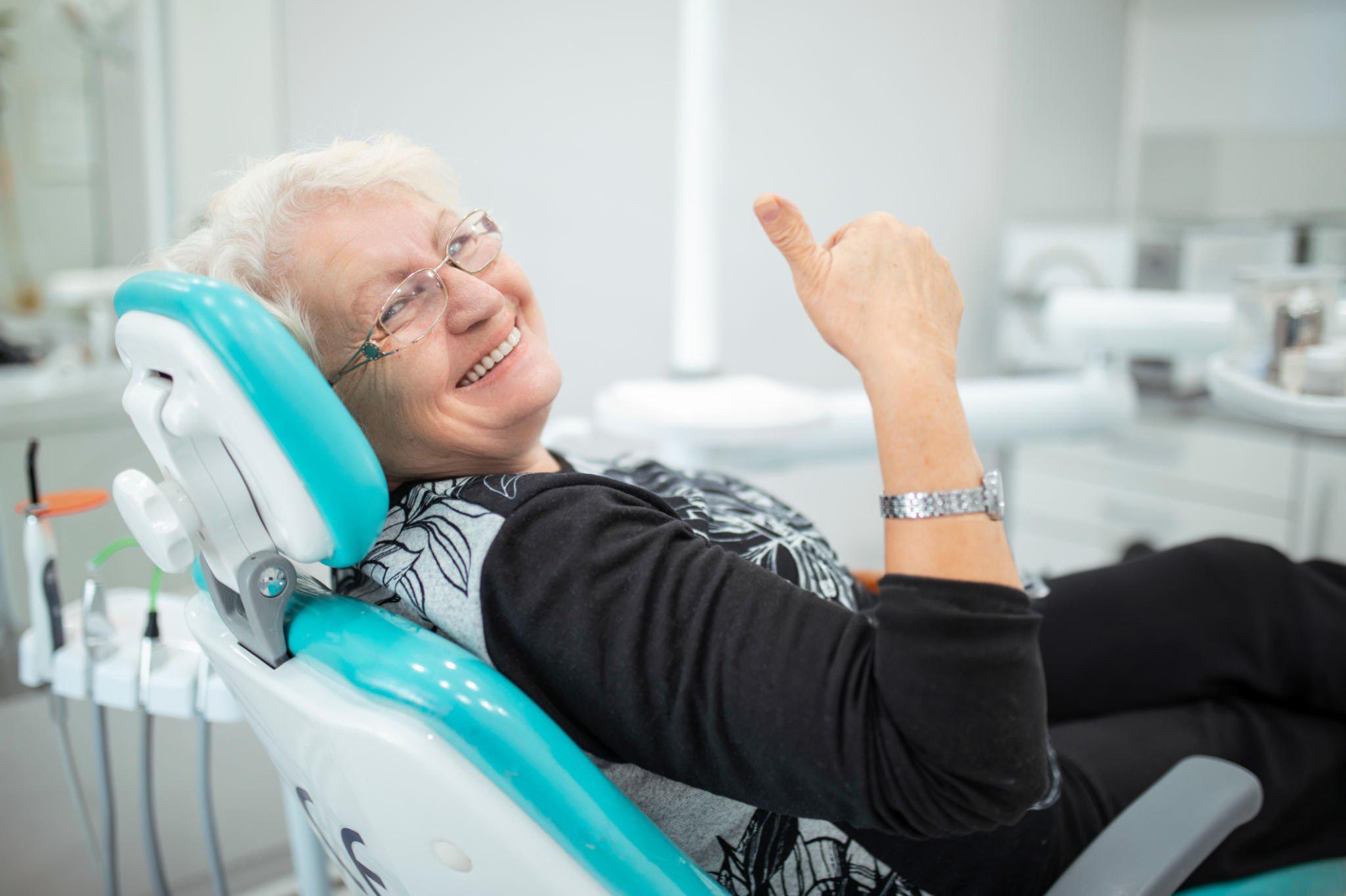 Smiling older woman in a dental chair giving a thumbs up