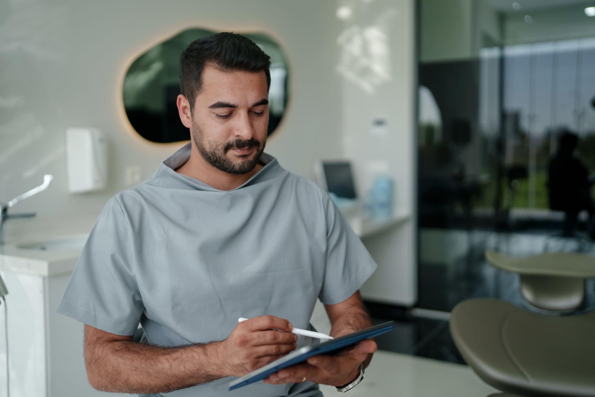 Man in scrubs writing on a tablet in a clinic room