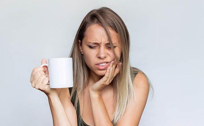 Woman holding her cheek in pain while holding a white mug