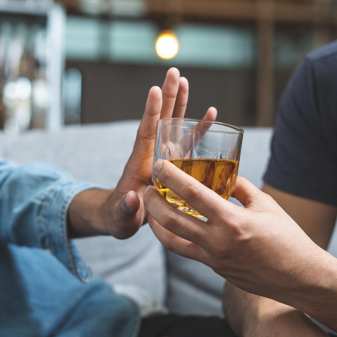 Hand pushing away a glass of whisky