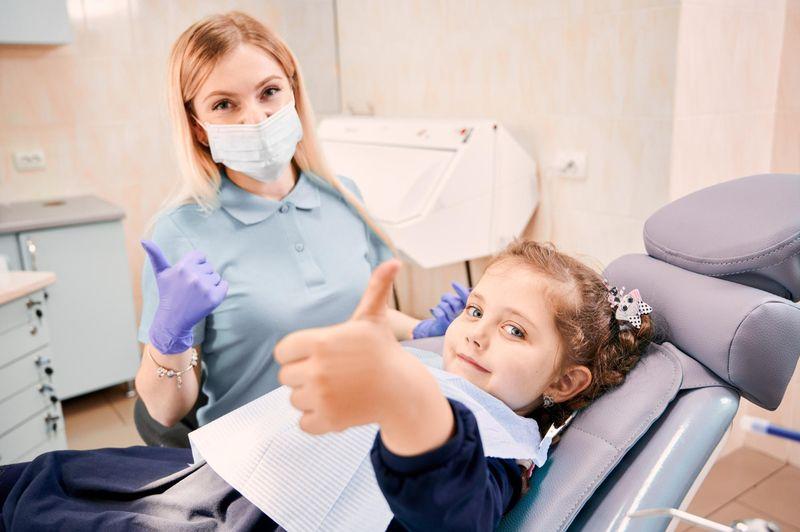 Dentist and a girl both giving thumbs up in a dental chair