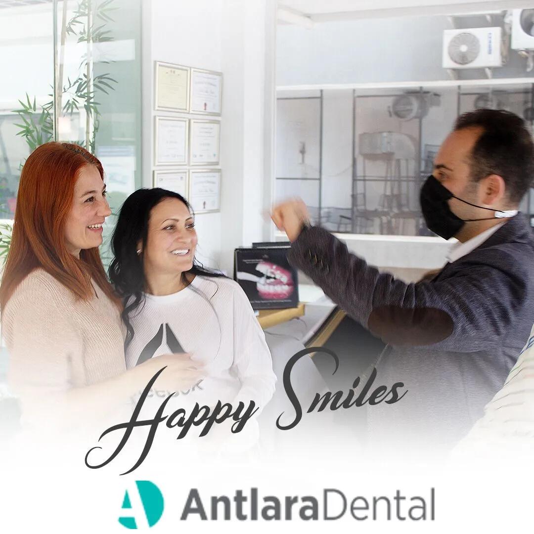 Two patients smiling while a masked dentist talks to them