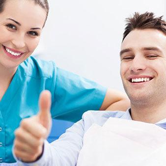 Dental assistant and patient smiling and giving a thumbs up