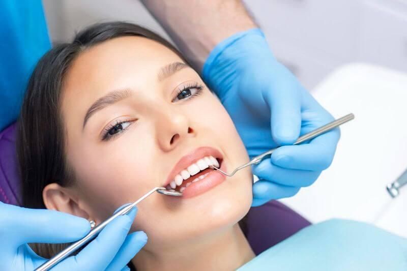 Patient smiling during a teeth whitening procedure, with the dentist's gloved hands