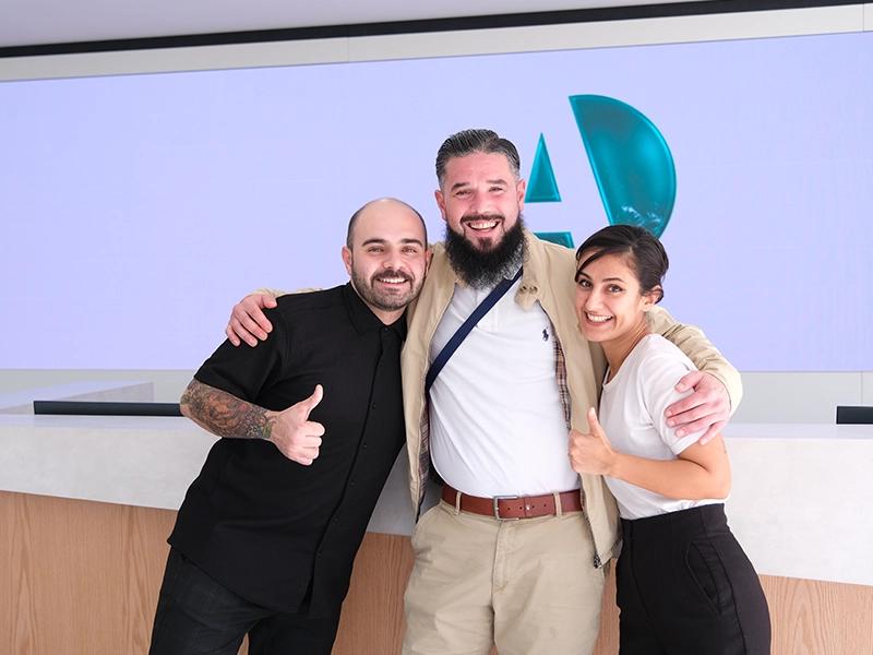 Three smiling people giving thumbs up at a clinic reception desk