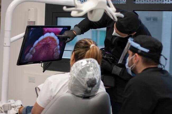 Masked clinicians examining a patient with the mouth image shown on a screen
