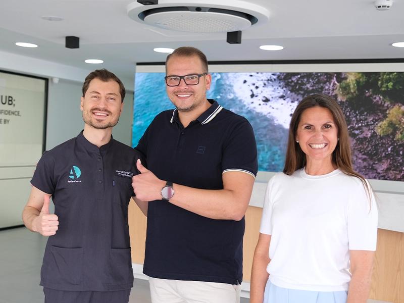 Three smiling people giving thumbs up in a clinic lobby