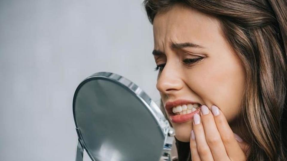 Woman with tooth pain looking in a hand mirror