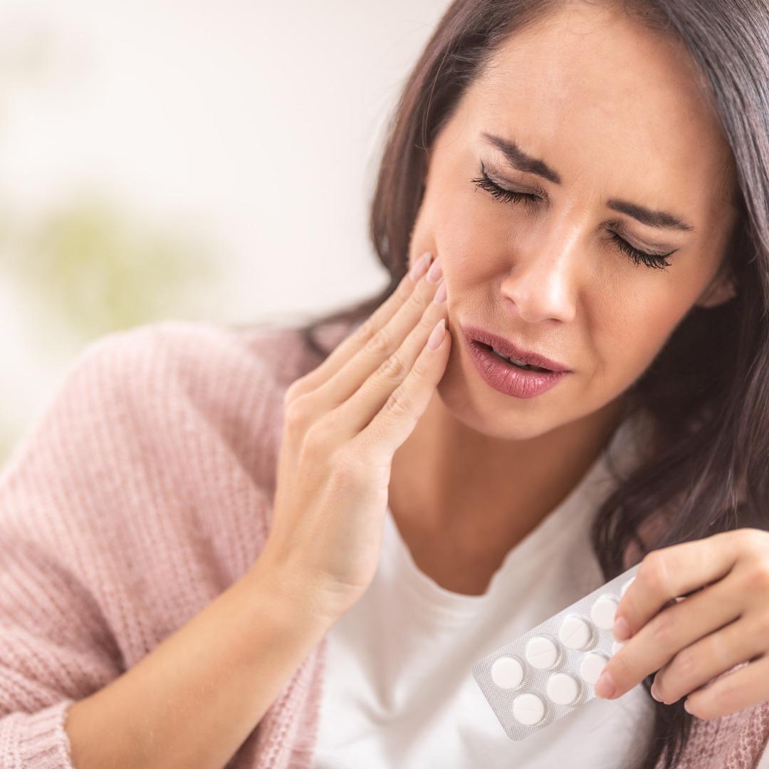 Woman holding her cheek and a blister pack of tablets