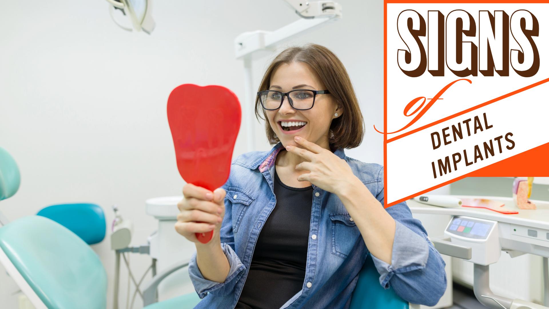 Woman in a dental chair smiling into a hand mirror