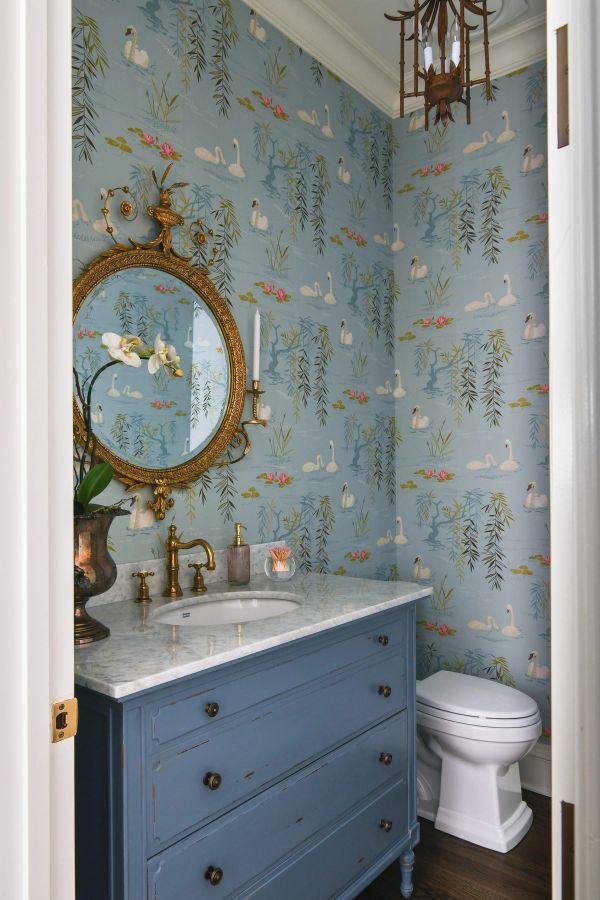 Powder room with whimsical blue swan-patterned wallpaper, blue-gray marble-topped vanity, and ornate gold-framed mirror