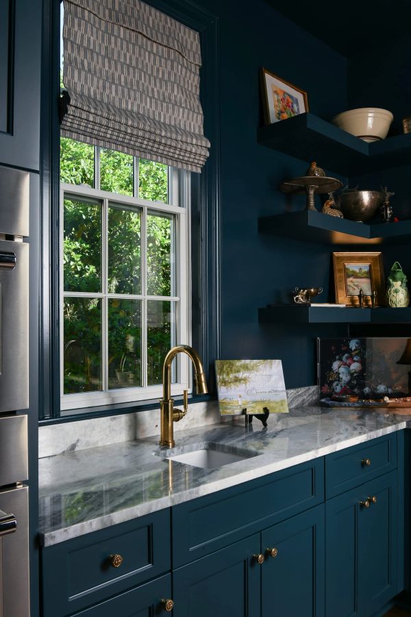 Butler's pantry detail featuring dark teal cabinets, marble countertops, brass gooseneck faucet, and floating shelves with art and silver decor