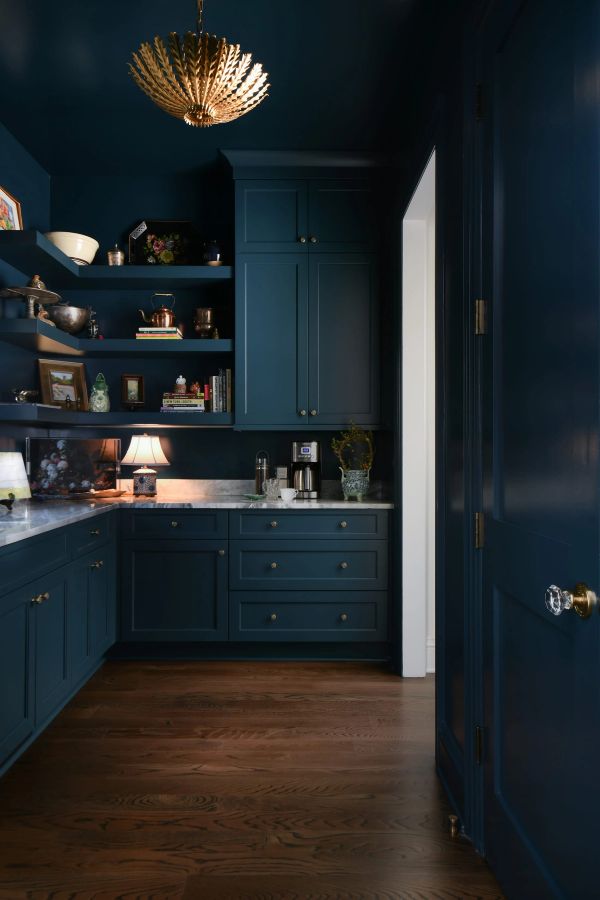 Moody navy blue butler's pantry with marble countertops, open shelving, brass chandelier, and styled vintage decor