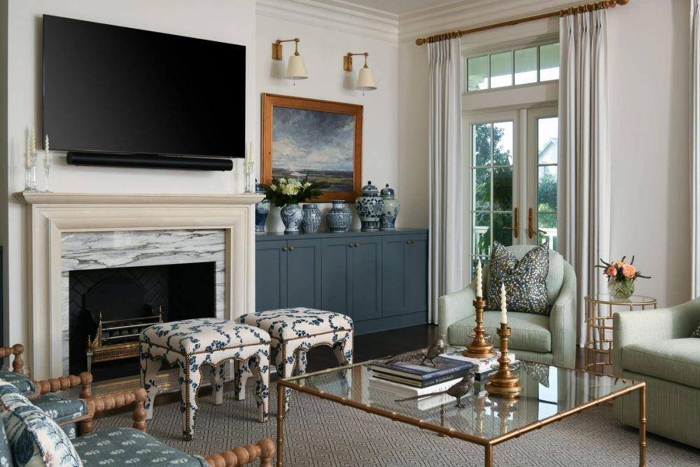Elegant living room featuring a marble fireplace, wall-mounted television, blue and white floral ottomans, and slate-blue built-in cabinets with chinoiserie vases