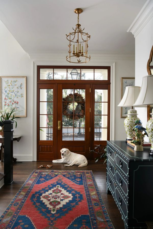 Bright home entryway featuring a wooden front door with a leaf wreath, a colorful patterned runner rug, and a gold birdcage chandelier