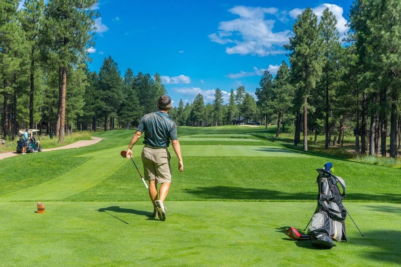 A golfer walking down a tree-lined fairway carrying a driver
