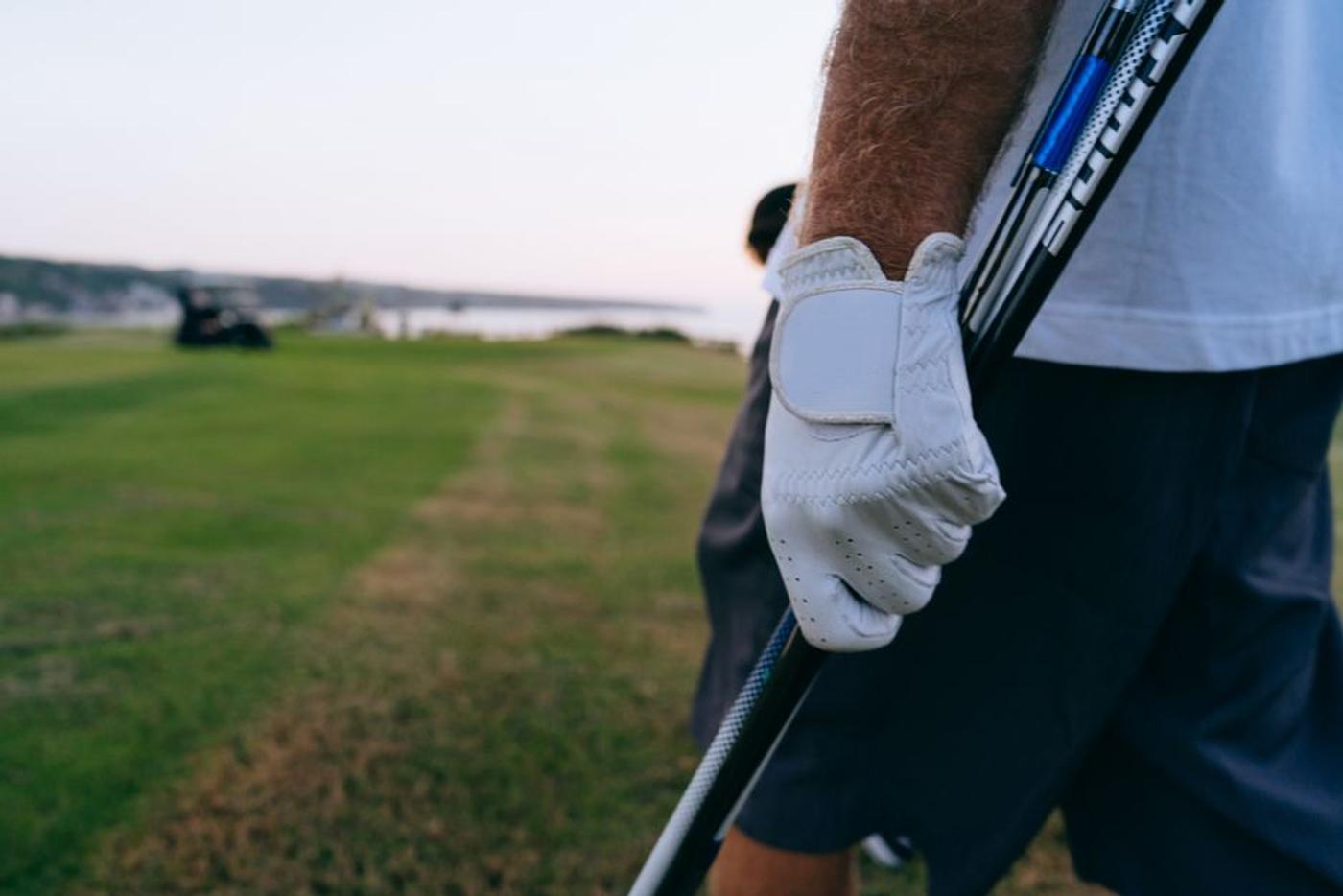 Close-up of a golfer's gloved hand holding a club on a beautiful golf course.
