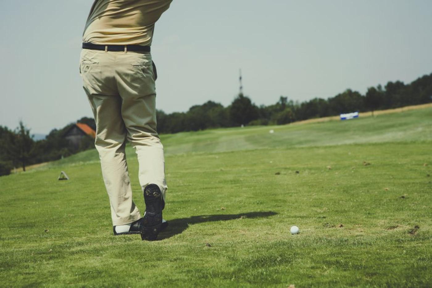 Golfer taking a swing on a sunny day, showcasing leisure and sport on a lush golf course.