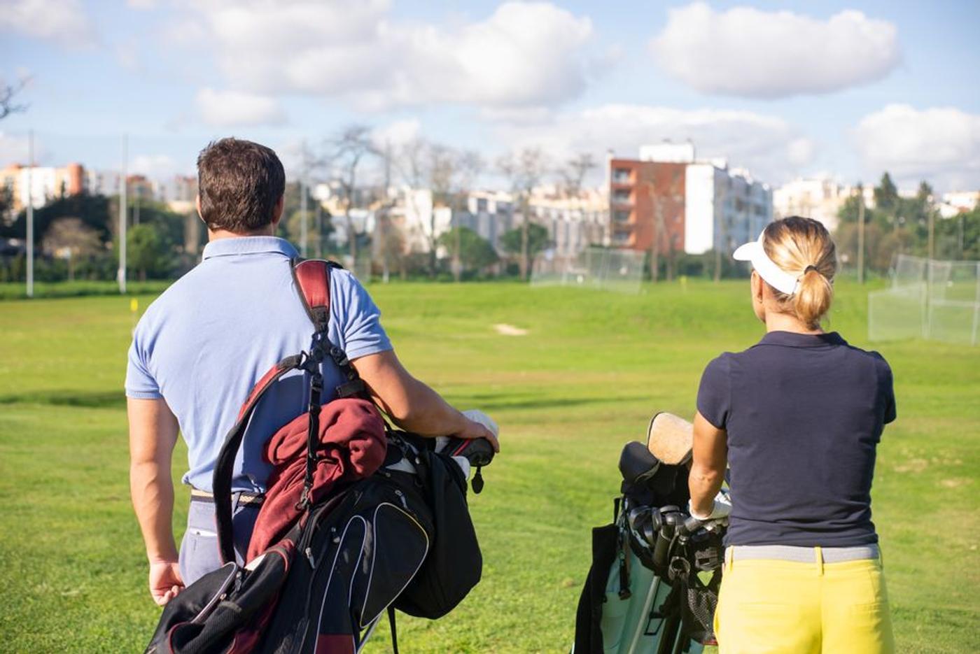 A man and woman carrying golf bags on a sunny day at a golf course in Portugal.