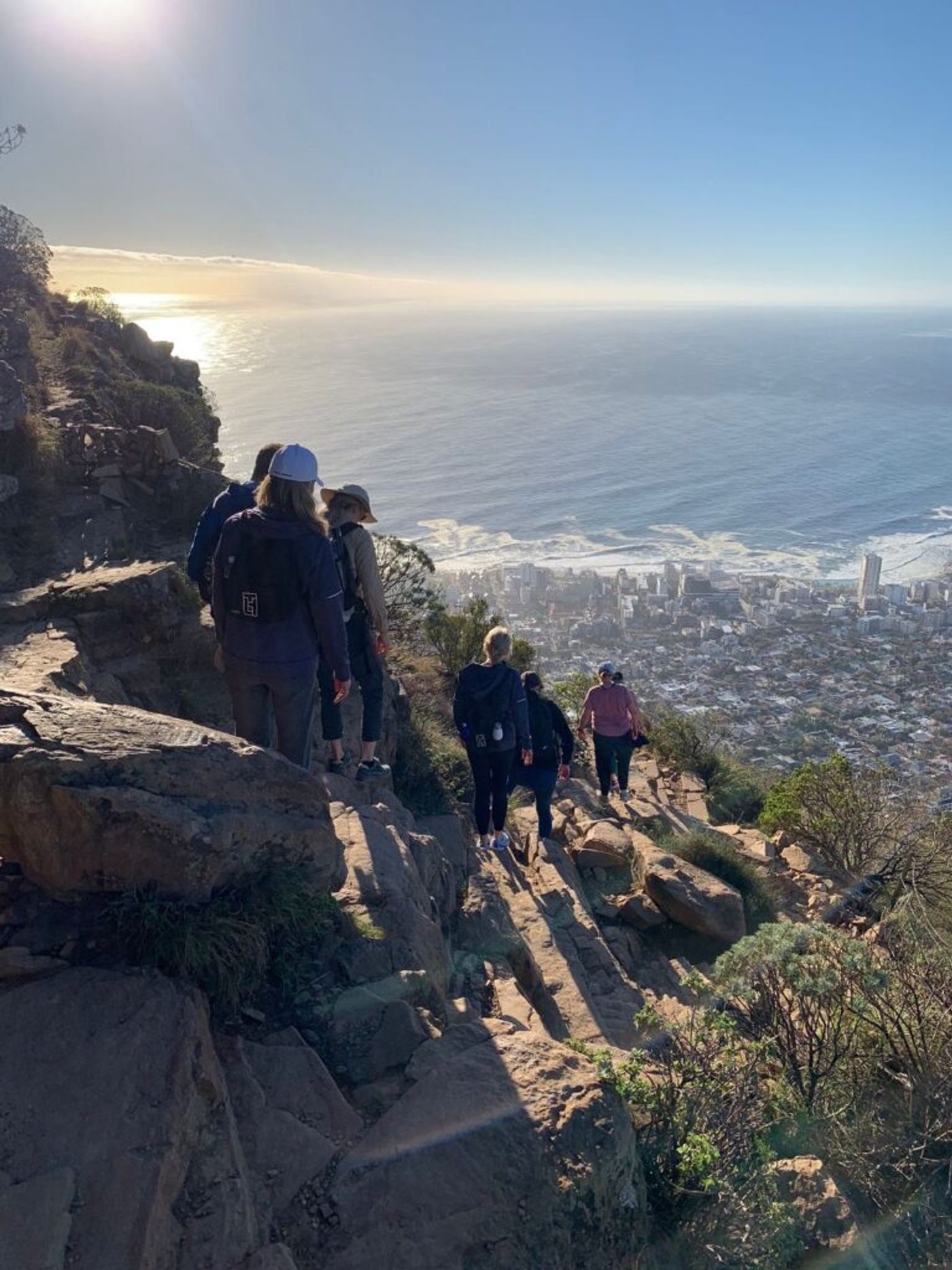 A group of walkers climbing a rocky mountain path above the sea at sunrise