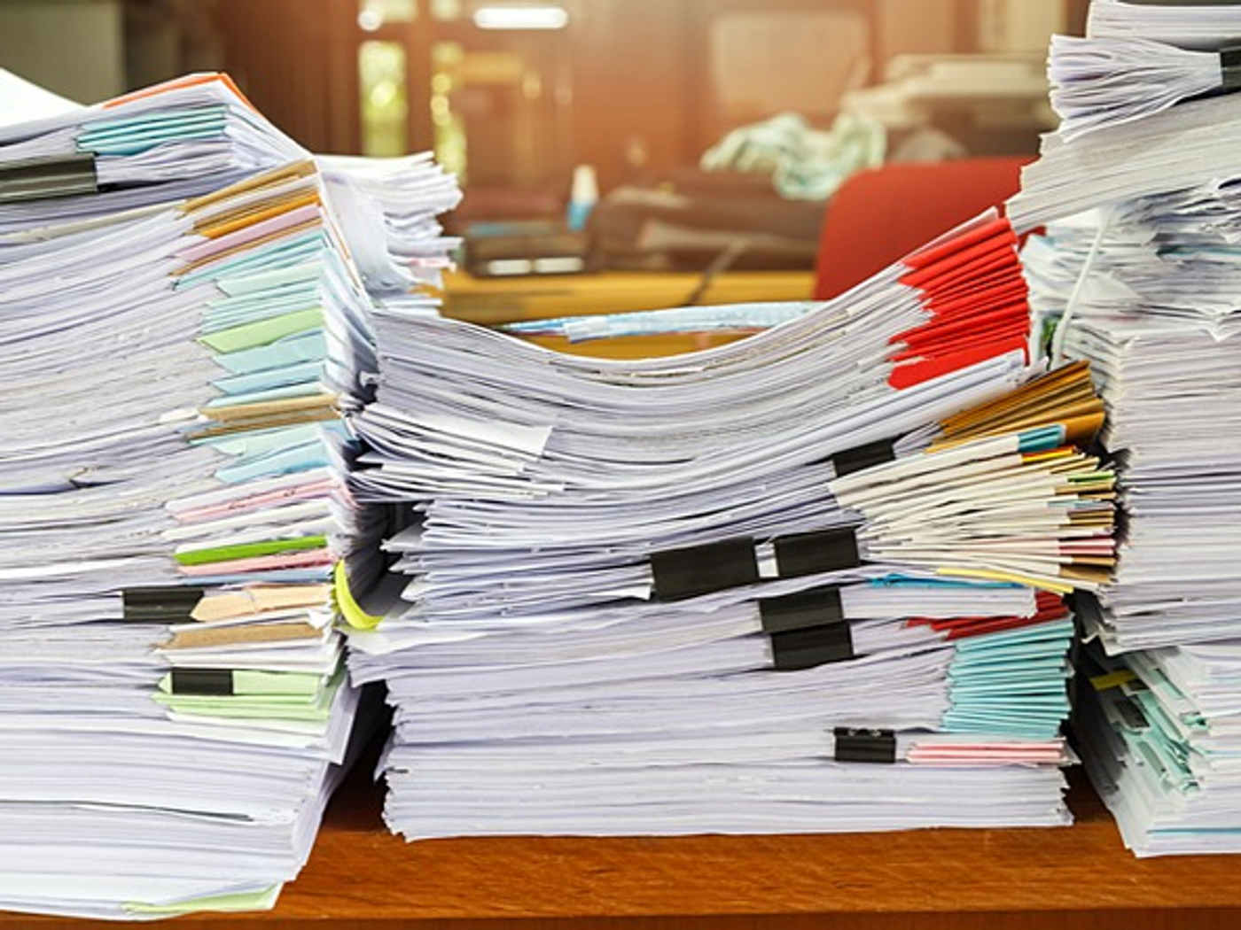Tall stacks of paperwork and files piled on a desk