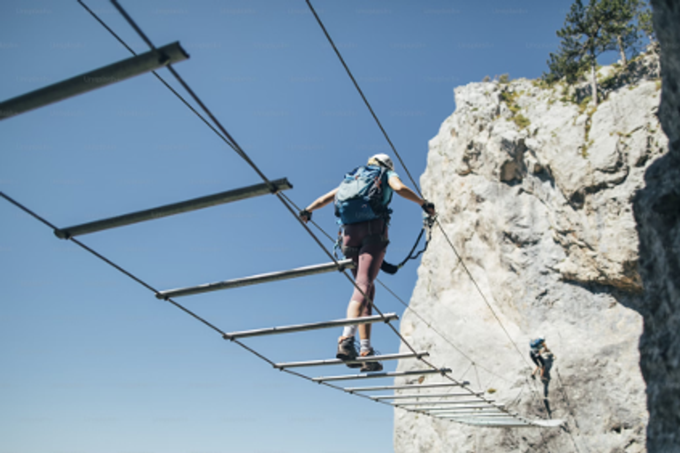 A climber crossing a suspended ladder bridge between rock faces